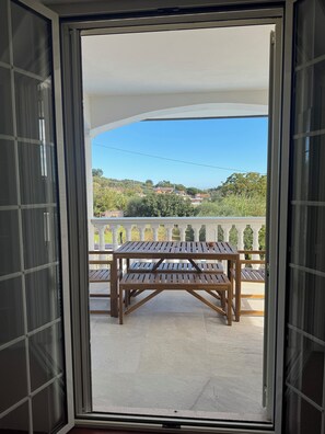 A balcony with a wooden table and chairs, a white balustrade, and a view of greenery and buildings. - ROME - Spacious apartment in a villa with a pool and barbecue, 1 km from the sea (Riccio)