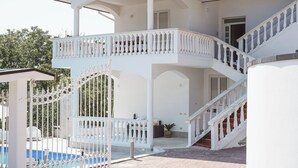 Um edifício branco com área externa coberta, piscina e escadaria.