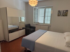 A bedroom with a bed, a chair, a wardrobe, and a window with blinds. - ROME - Spacious apartment in a villa with a pool and barbecue, 1 km from the sea (Riccio)