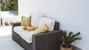 Um sofá de vime com almofadas brancas e um cobertor amarelo, posicionado ao lado de um vaso de planta.