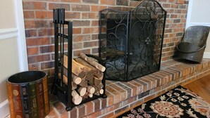 A brick fireplace with a metal screen, a stack of firewood, and a decorative metal chair. - Riverside Getaway - Enjoy Quiet Life Right on the Duck River (Shelbyville)