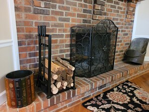 Cozy space with a brick fireplace, decorative metal screen, and a black metal bookstand.