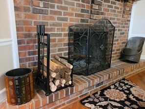 Cozy space with a brick fireplace, decorative metal screen, and a black metal bookstand.