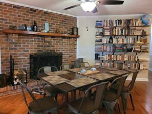 Cozy dining area with a brick fireplace, large dining table, and bookshelf for a relaxing atmosphere.