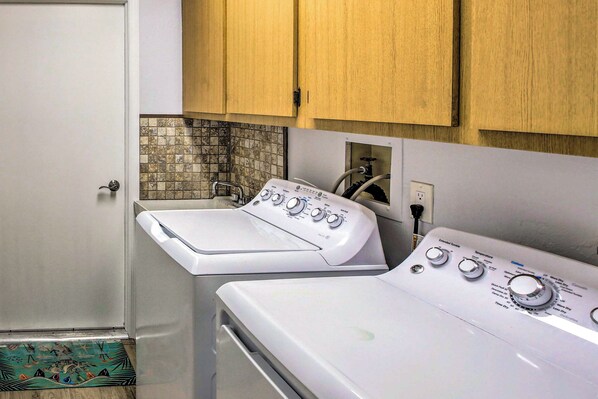 A laundry room with two white washing machines, wooden cabinets, and a tiled backsplash.