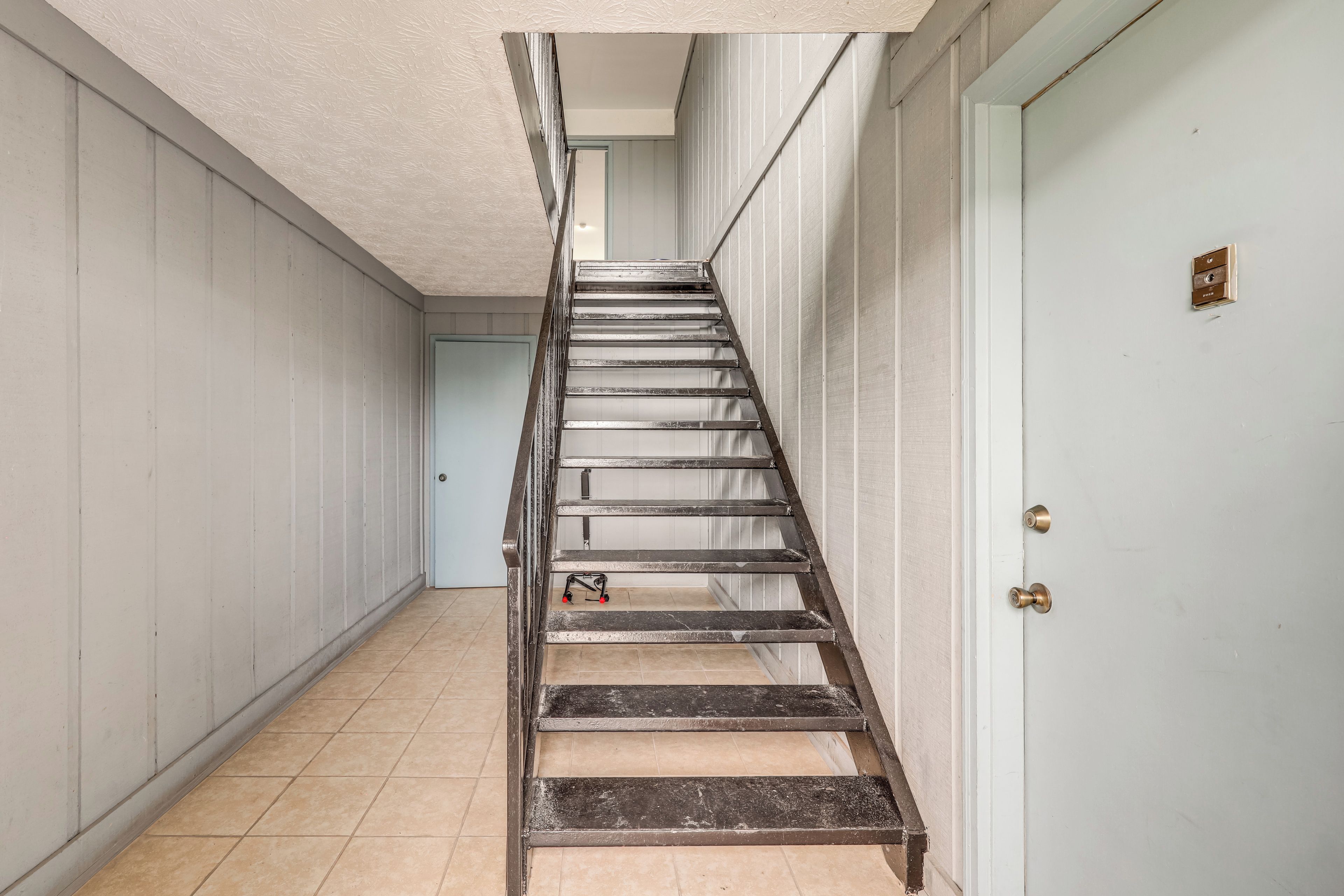 Un couloir étroit avec un escalier en métal menant à une porte dotée d’une poignée de porte en laiton.