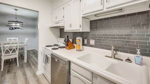 A kitchen with white cabinets, a stainless steel dishwasher, a white sink, and a grey tiled backsplash. - < Half-Mi to Fort Clinch Beach! Condo w/ Balcony (Fernandina Beach)