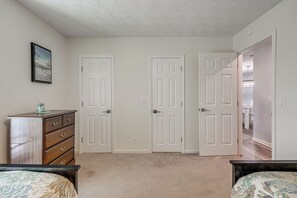 A bedroom with two doors, a dresser, a bed, and a hallway leading to another room.