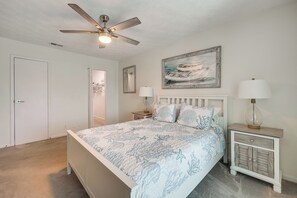 A bedroom with a bed, a ceiling fan, a nightstand with a lamp, a painting on the wall, and a door. - < Half-Mi to Fort Clinch Beach! Condo w/ Balcony (Fernandina Beach)