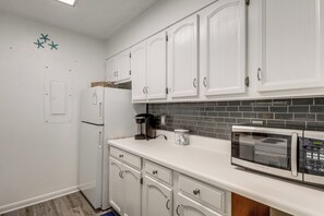 Eine Küche mit weißen Schränken, einem Kühlschrank, einer Kaffeemaschine, einer Mikrowelle und einer gefliesten Spritzschutzwand.
