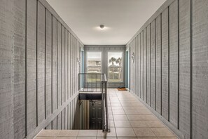 Un pasillo estrecho con vista al exterior, una puerta y una pequeña mesa.