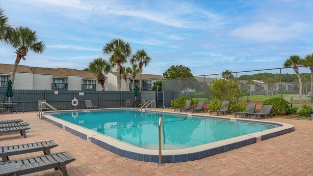 A swimming pool with a brick deck, lounge chairs, and palm trees. - < Half-Mi to Fort Clinch Beach! Condo w/ Balcony (Fernandina Beach)