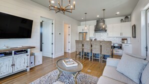 A modern living room with a flat-screen TV, a coffee table with books, a sofa, and a chandelier. - Luxe Beachfront WindMark Cottage w/ Deck! (Port St. Joe)