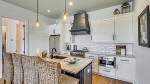 A modern kitchen with white cabinetry, a central island, stainless steel appliances, and a hanging light fixture. - Luxe Beachfront WindMark Cottage w/ Deck! (Port St. Joe)