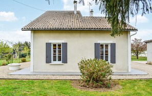 Ein eingeschossiges Haus mit Ziegeldach, zwei Fensterläden und ein kleiner Busch im Vorgarten.