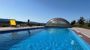 A clear blue pool with a glass enclosure, surrounded by a deck with chairs and a view of distant hills. - Villa-view, Pool, Bbq, Playground & Fire pit (Horni Plana)