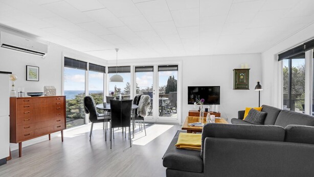A modern living room with a grey sofa, wooden cabinet, and a dining area with chairs and a table. - Amazing home in Allinge with kitchen (Allinge)