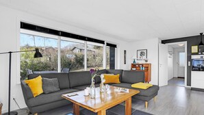 A modern living room with a grey sofa, wooden coffee table, and a view of the outdoors through large windows. - Amazing home in Allinge with kitchen (Allinge)