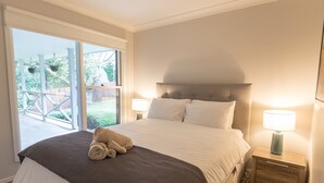 A bedroom with a large bed, a nightstand with a lamp, and a sliding glass door leading to an outdoor area. - The Grange country retreat, with a birds eye view! (Mittagong)