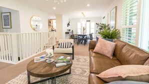 A spacious living room with a brown leather sofa, a round coffee table, and a dining area in the background. - The Grange country retreat, with a birds eye view! (Mittagong)