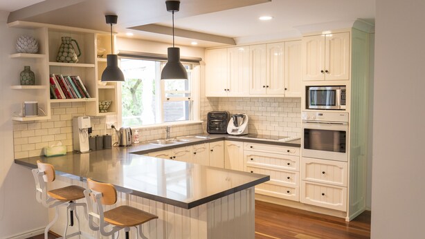 A modern kitchen with white cabinetry, a central island with bar stools, a microwave, oven, and a coffee maker. - The Grange country retreat, with a birds eye view! (Mittagong)