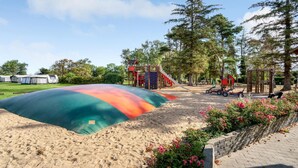 A playground with a colorful slide and climbing structures, surrounded by trees and a sandy area.