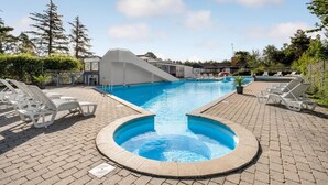 A swimming pool with a slide, lounge chairs, and a brick patio.