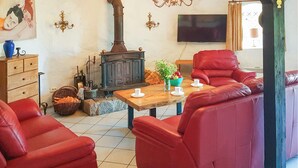 A living room with red leather sofas, a wooden table with cups, a vintage stove, and a television on the wall. - 3 bedroom amazing home in Sterlawki Male (Sterlawki Male)