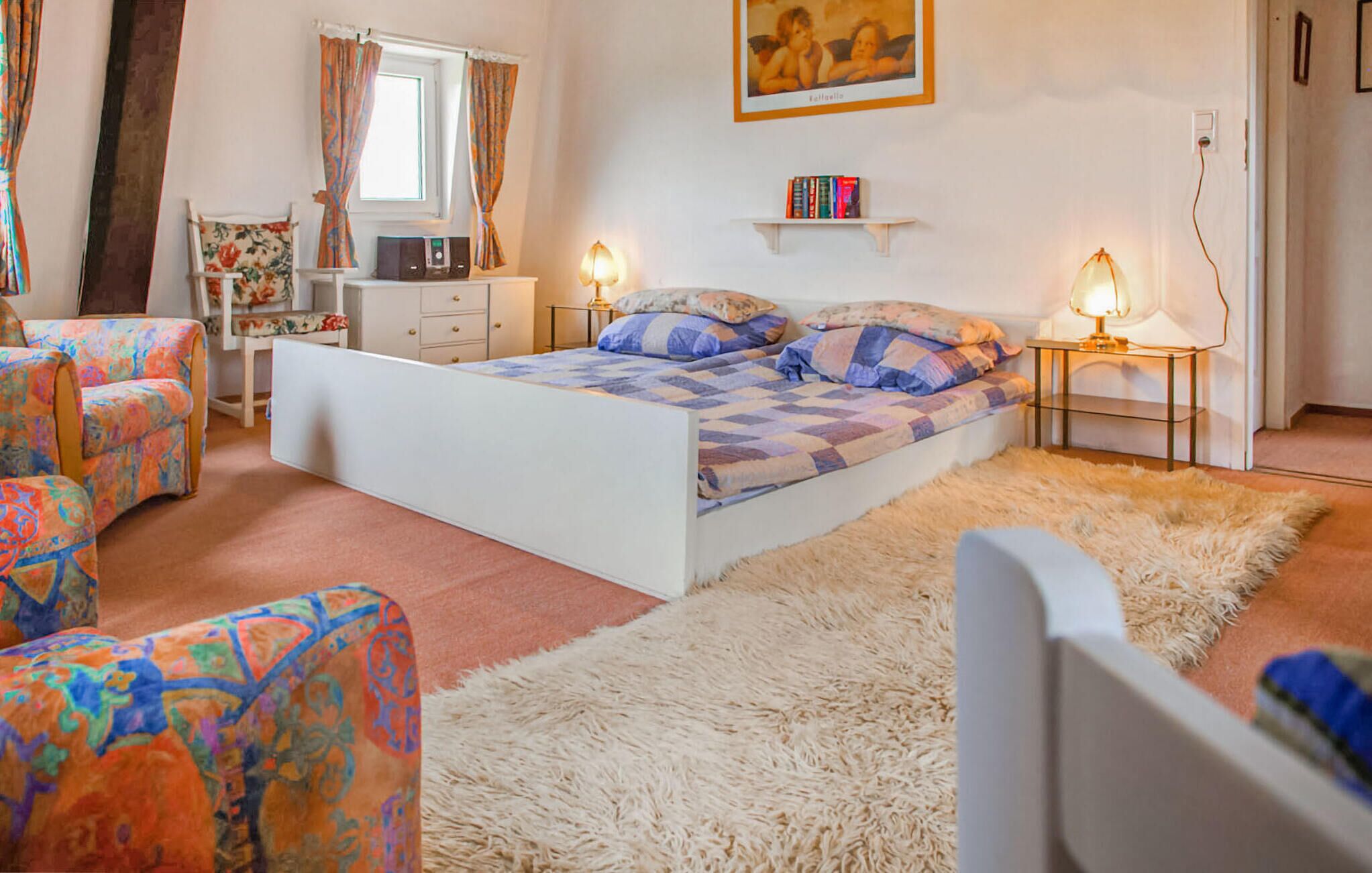 Une chambre à coucher avec un lit, deux tables de chevet, une chaise, une petite armoire blanche, un tapis moelleux et un tableau accroché au mur.