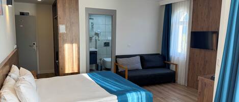 Habitación de hotel con cama, sofá, televisión y baño visible a través de una puerta abierta.