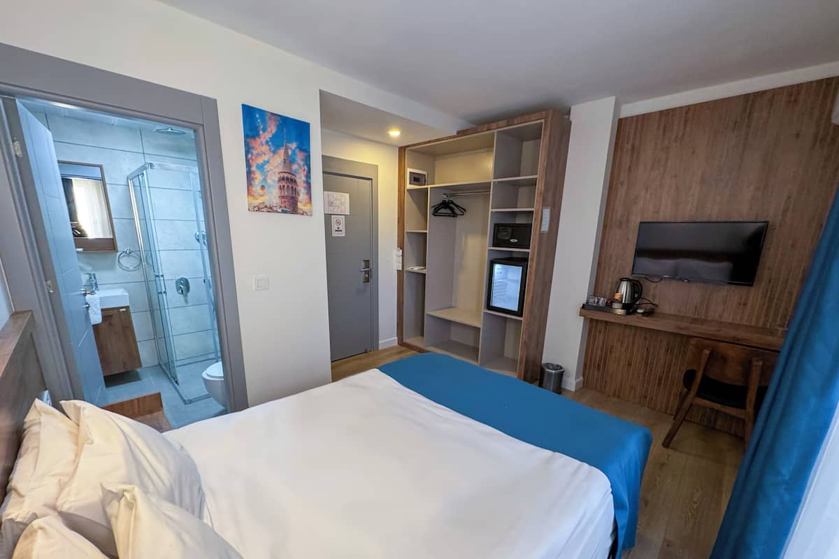 A hotel room with a bed, a desk, a TV, a wardrobe, and a bathroom.