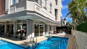 A poolside view of a hotel with a large pool, outdoor seating, and a multi-story building with balconies. - Premier Inn City  (Antalya)