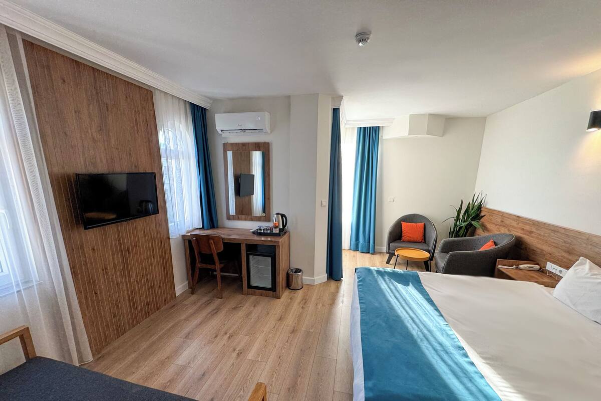 A hotel room with a bed, desk, chair, TV, and a small table with a plant.