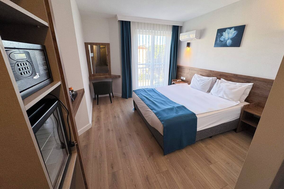 A hotel room with a bed, a desk, a chair, a telephone, and a wall-mounted air conditioner.
