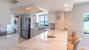 Een moderne keuken met een groot eiland, roestvrijstalen apparatuur en uitzicht naar buiten.