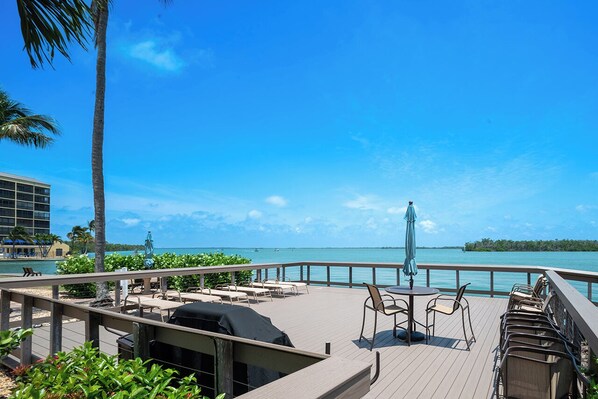 A deck with outdoor seating, a grill, and a view of the ocean.