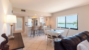 Een moderne woonkamer met een eethoek, een keuken op de achtergrond en een groot raam met uitzicht.