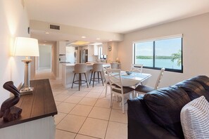 A modern living room with a dining area, a kitchen in the background, and a large window with a view.