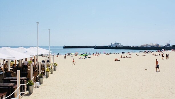 A beach with umbrellas and tables, a pier in the background, and a ship docked. - Apartment facing pier with sea view, WIFI and secure parking space (Quiberon)