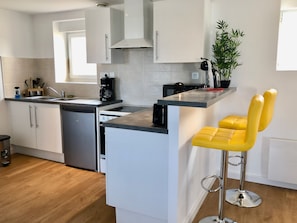 A modern kitchen with white cabinetry, a built-in dishwasher, a coffee maker, and a bar stool with yellow seats.