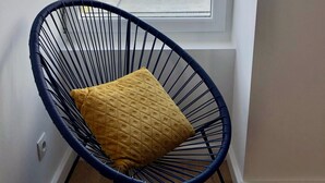 A corner room with a large window, a blue wire chair with a yellow cushion, and a view of a distant shoreline. - Apartment facing pier with sea view, WIFI and secure parking space (Quiberon)