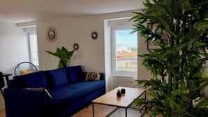 A living room with a blue sofa, a wooden coffee table, and a large green plant. - Apartment facing pier with sea view, WIFI and secure parking space (Quiberon)