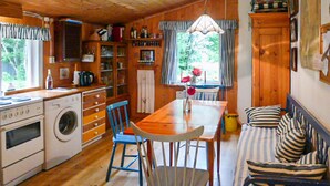 A cozy cabin-style room with a wooden interior, a dining table with chairs, a sofa, and a kitchen area with a washing machine. - Cozy home in Dals-Rostock with kitchen (Dals-Rostock)
