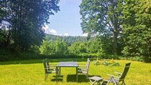 An outdoor seating area with a table and chairs on a grassy field, surrounded by trees and a mountain in the background. - Cozy home in Dals-Rostock with kitchen (Dals-Rostock)