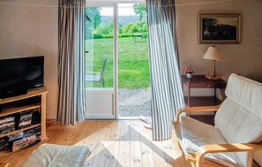Una sala de estar con televisor, sofá, sillón, mesa con lámpara y un cuadro en la pared.