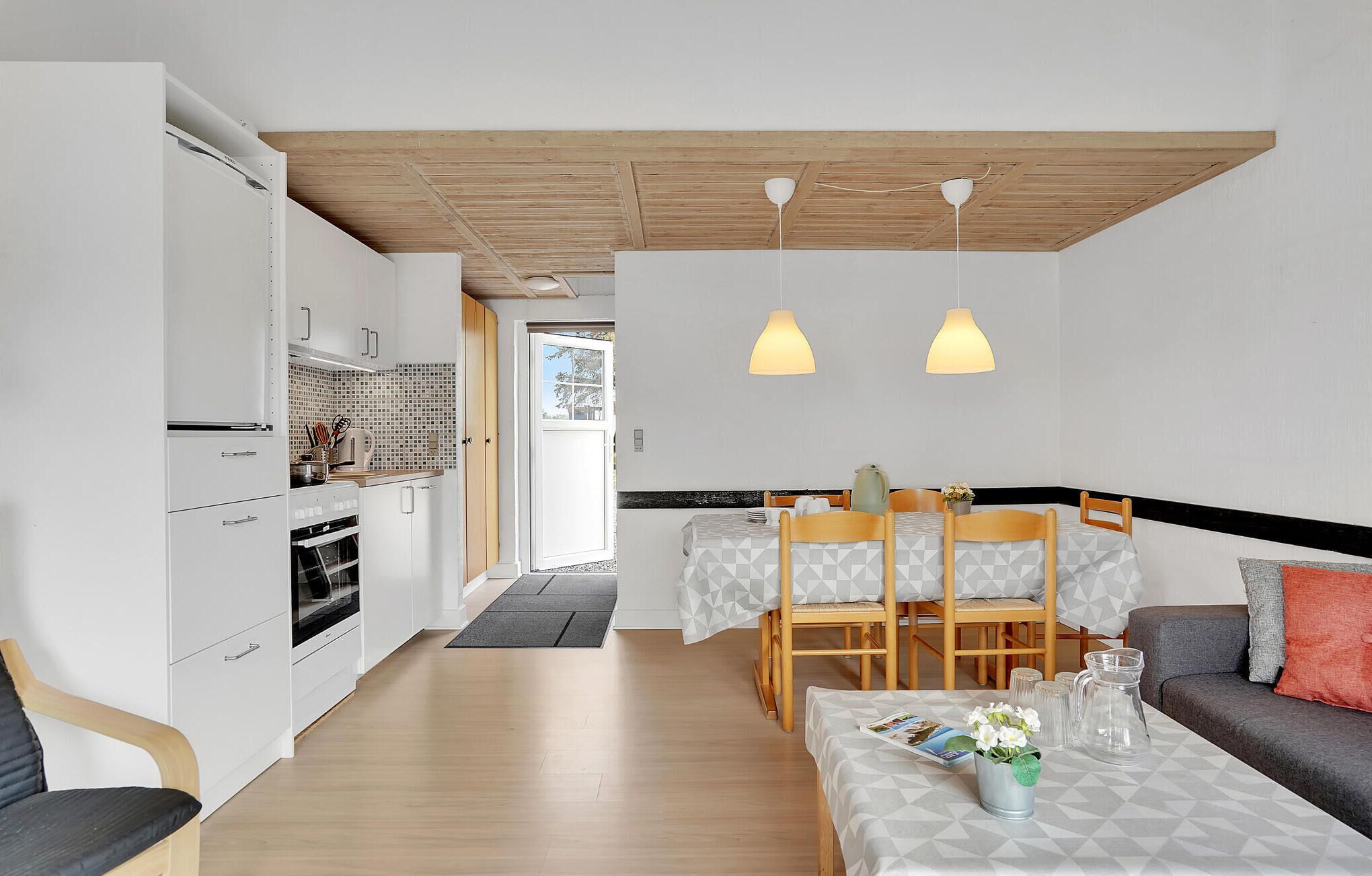 A modern kitchen with white cabinets and a tiled backsplash, a dining area with a table and chairs, and a living area with a sofa and a coffee table.