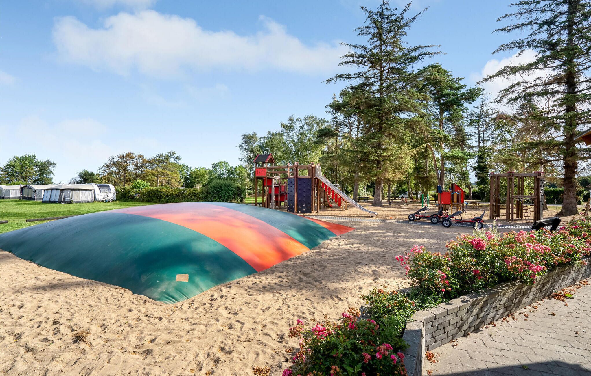 Un'area giochi con uno scivolo colorato e strutture per arrampicarsi, circondata da alberi e un’area sabbiosa.