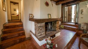 Una chimenea con detalles de piedra, una escalera que lleva a otra habitación y una silla de mimbre.