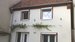 A two-story house with a white facade, brown trim, and a number '85' on the wall. There are three windows, one on each floor, and a door with a glass panel. - Vacation home "Lisbeth" (Edesheim)