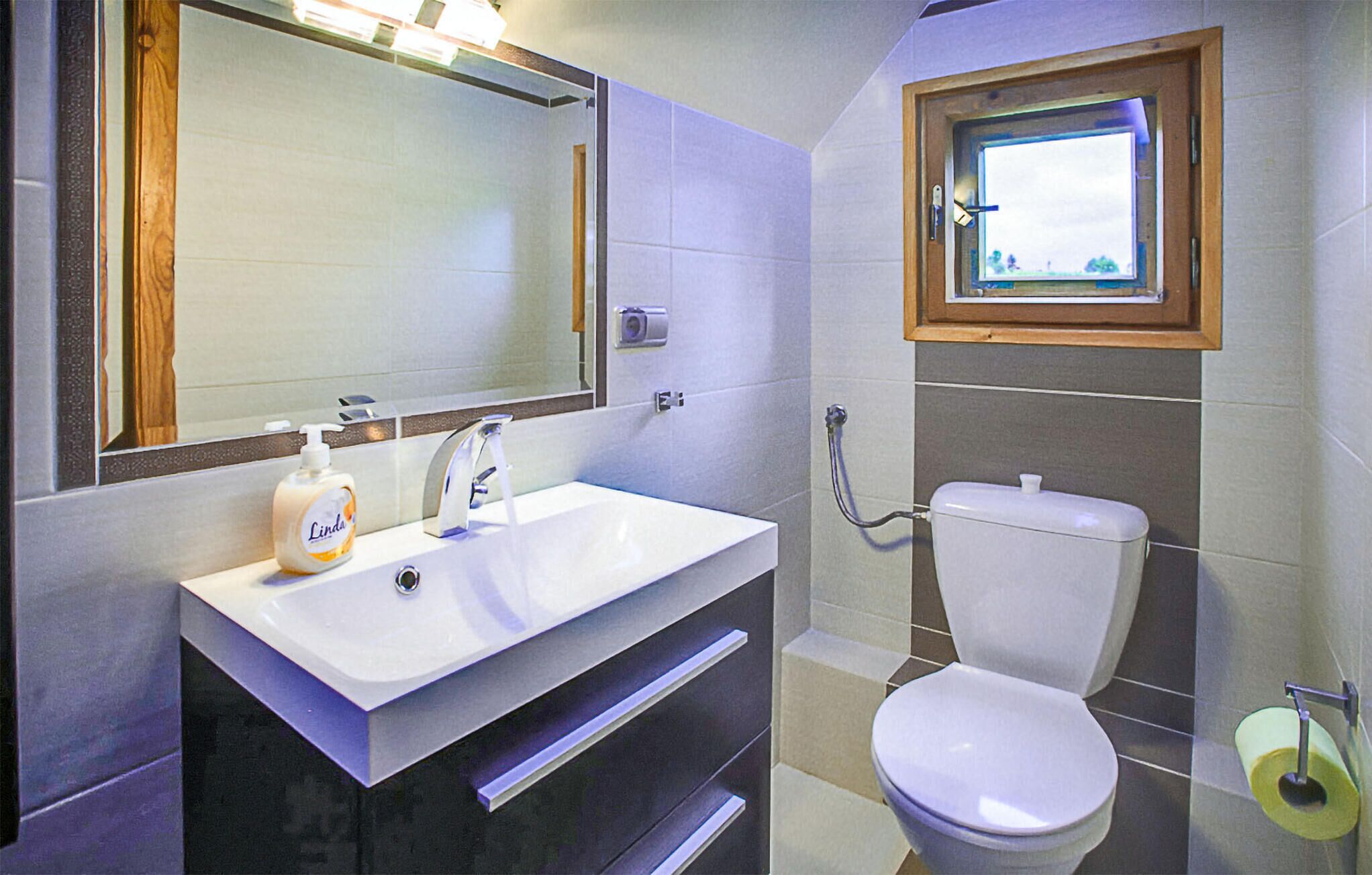 Un baño con lavamanos blanco, espejo, inodoro y ventana.